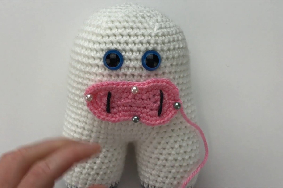 Pink crochet snout pinned onto the white amigurumi cow body