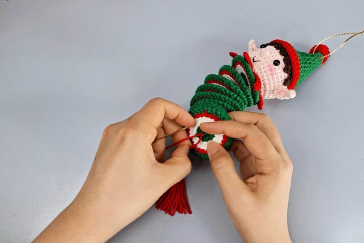 Sewing the crochet spiral wind spinner to the elf head with a red yarn tassel at the bottom