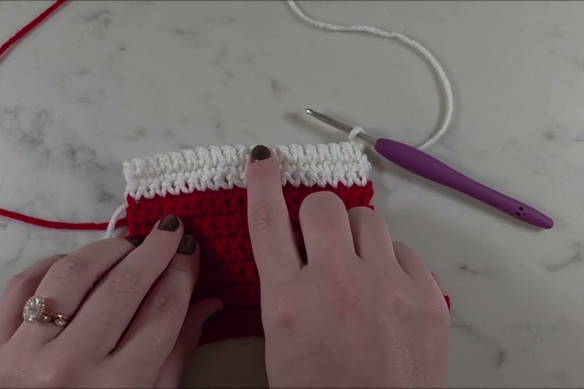 Red crochet mini stocking in progress with a white single crochet cuff and a purple-handled hook