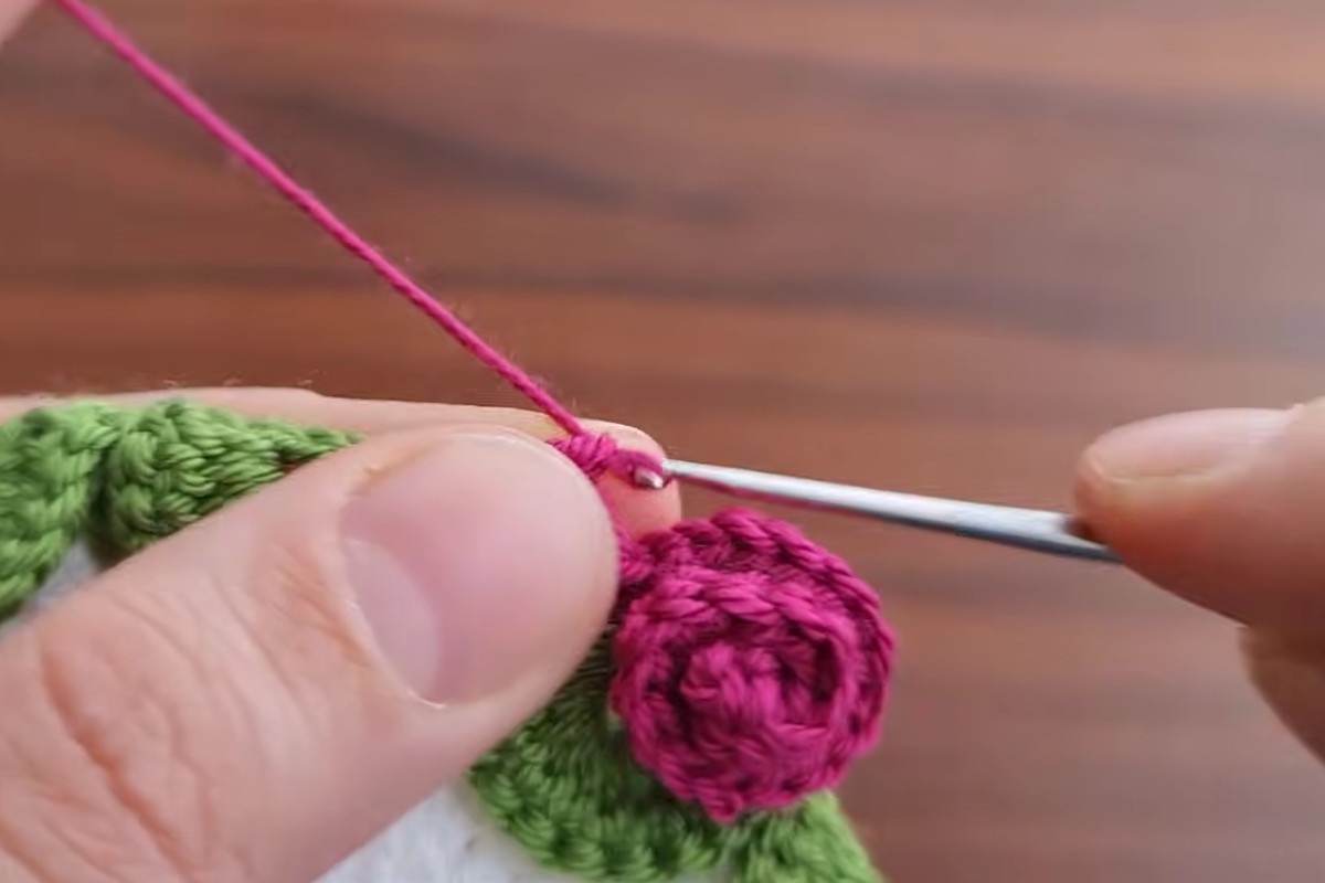 Crocheting a small pink rosette on the edge of the flower motif