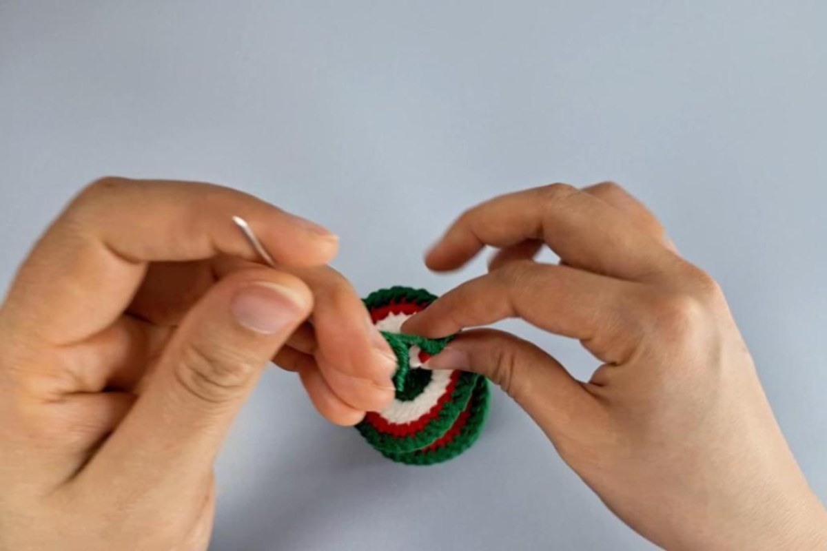 Red, white and green crochet spiral wind spinner body being worked with a yarn needle