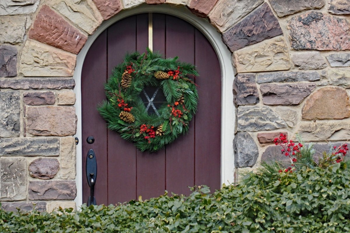 Evergreen Christmas wreath with pinecones on an arched wooden front door