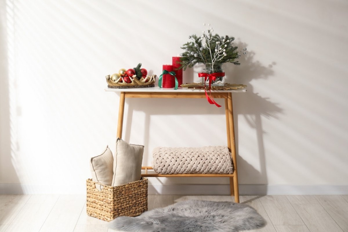 Entry console table decorated for Christmas with a small tree, candles and a basket underneath