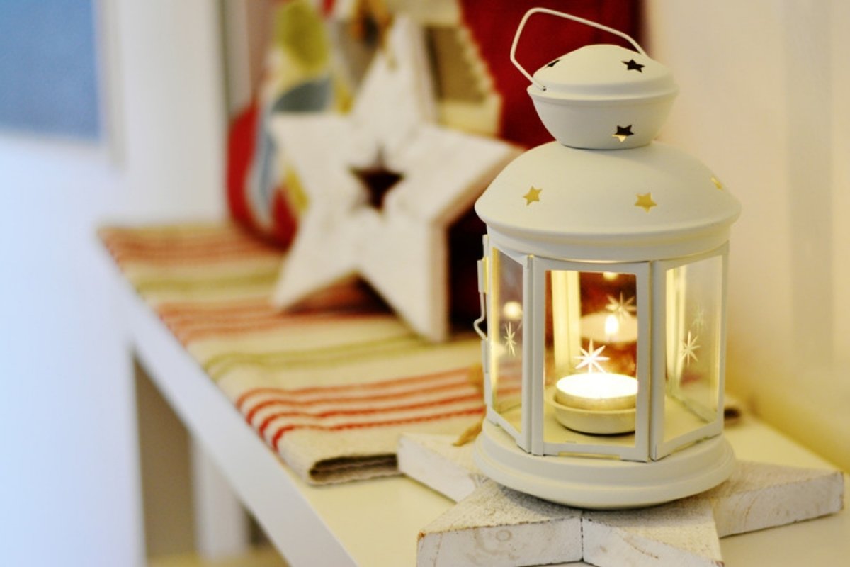 White lantern with a candle on a bench by a window for a cozy holiday entry