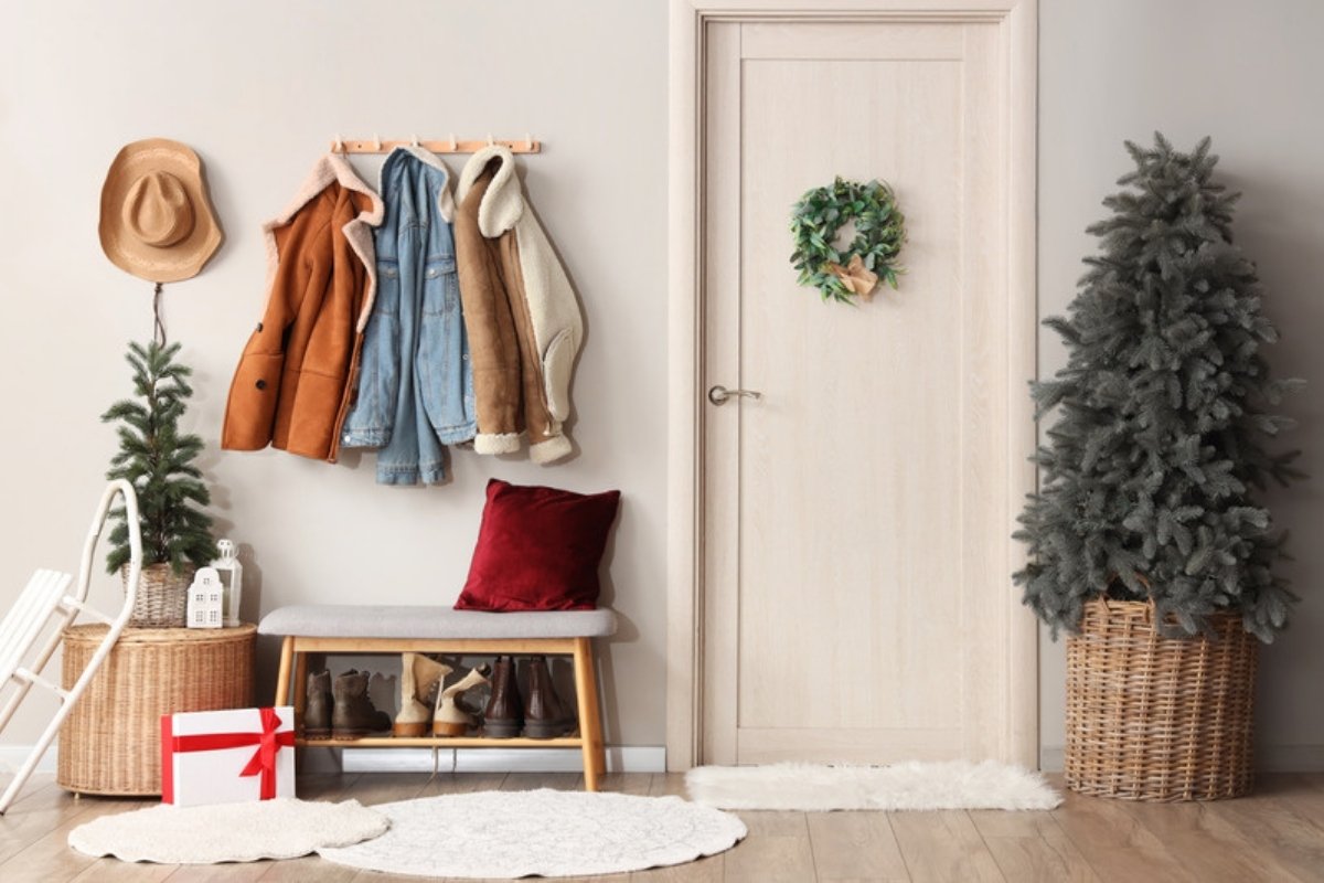 Christmas entryway with coat hooks, a storage bench for boots, a small wreath and potted trees