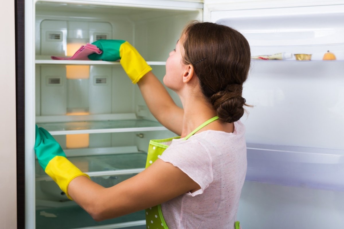 Woman wiping the shelves of an empty refrigerator