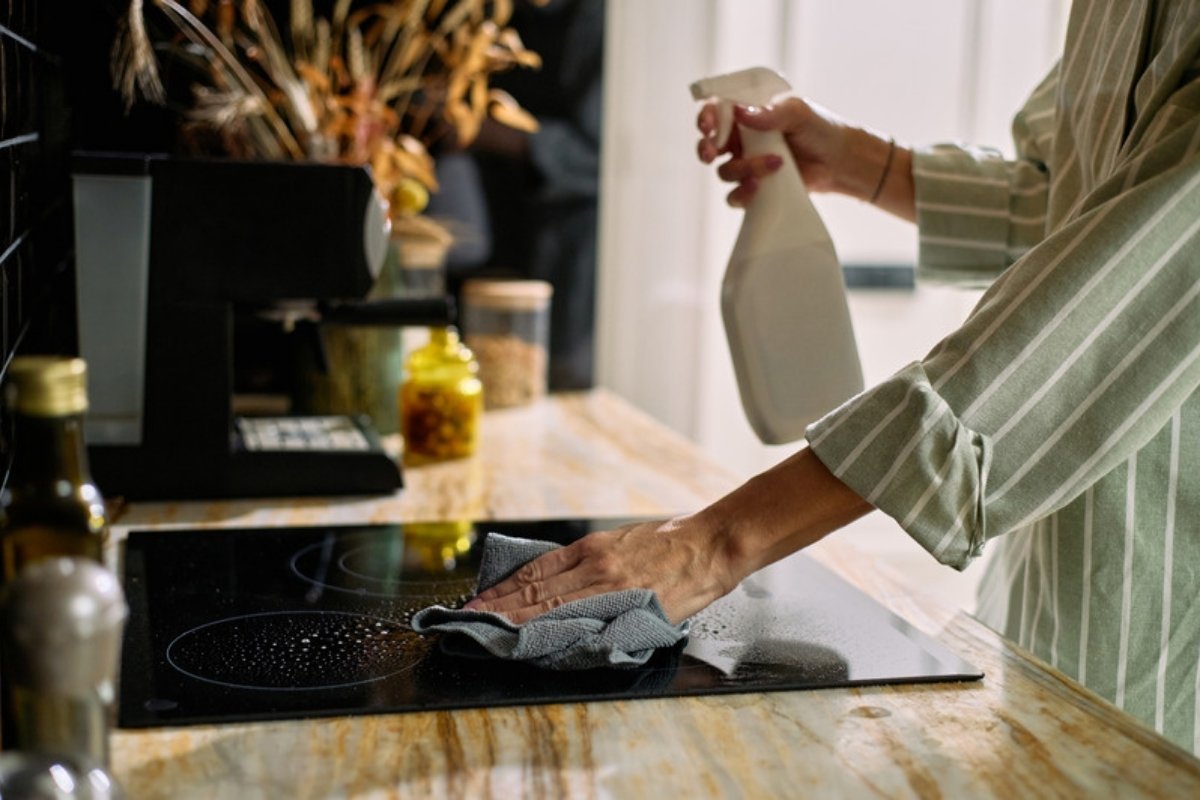 Wiping down a kitchen stovetop with a cloth and spray bottle