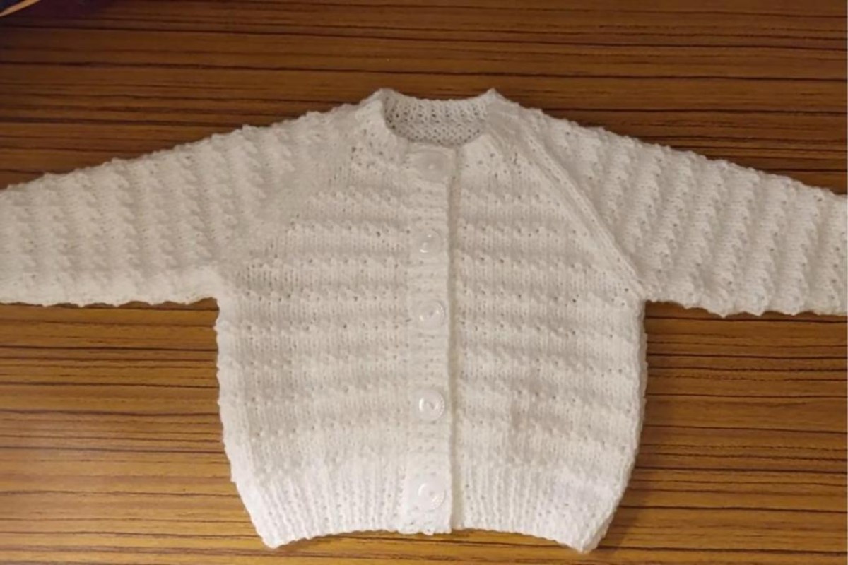 Finished white knitted baby cardigan with moss stitch stripes, raglan sleeves and buttons