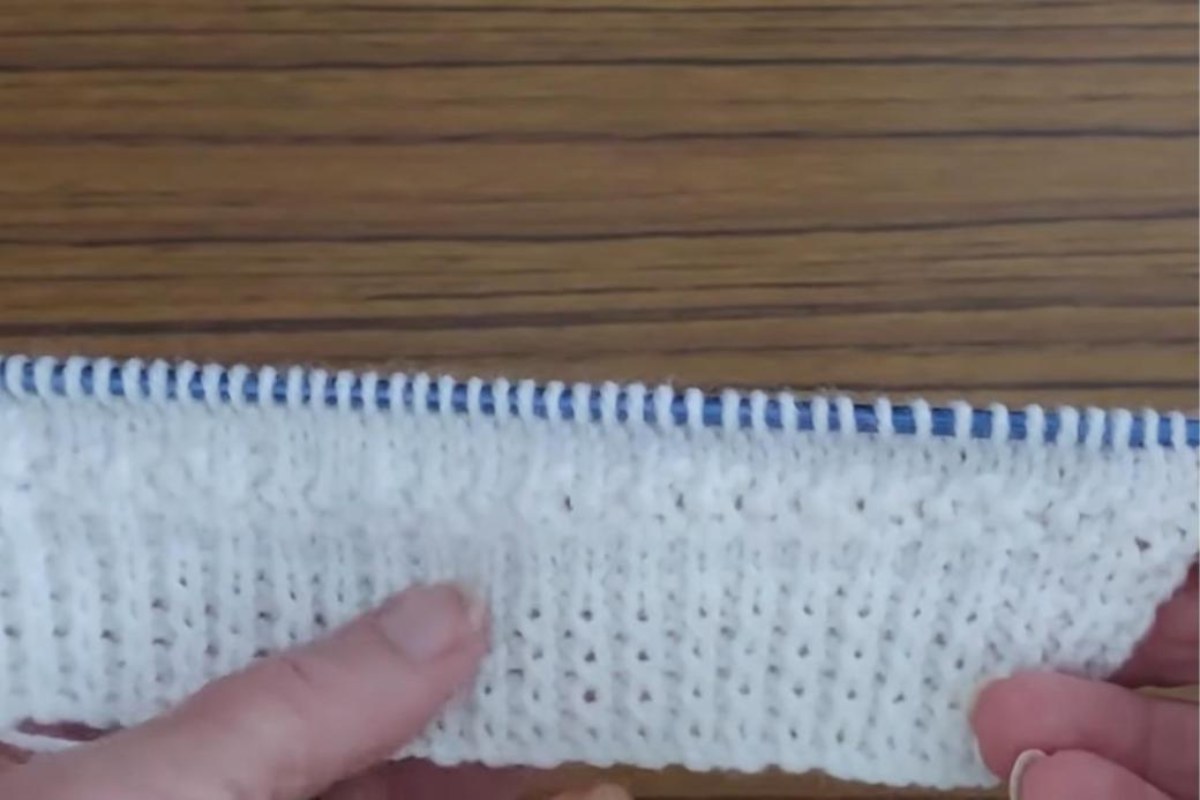 Back of the baby cardigan on the needles showing twisted rib and the moss stitch stripe pattern