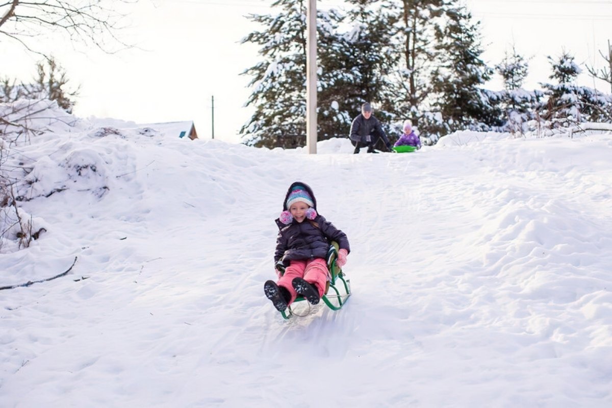 Child riding a sled feet first down a gentle snowy hill