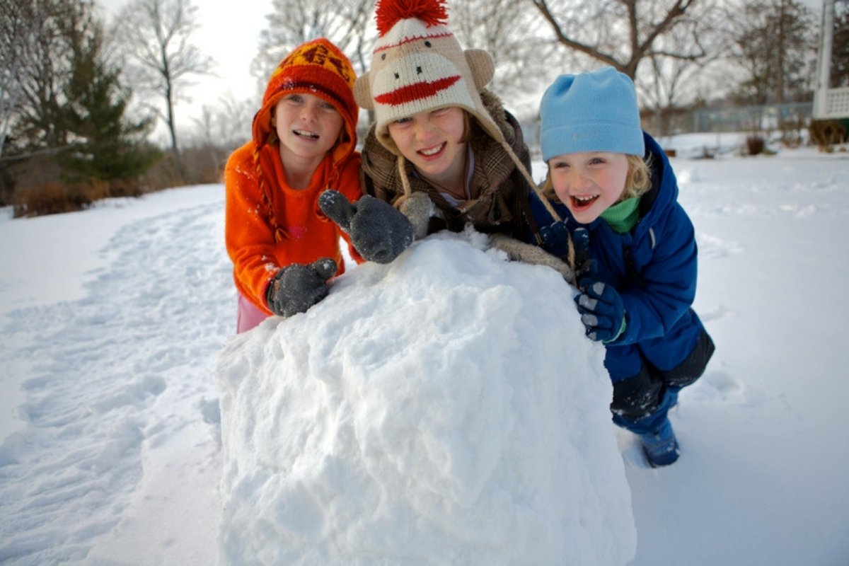 Three smiling kids leaning on a snow fort wall they built