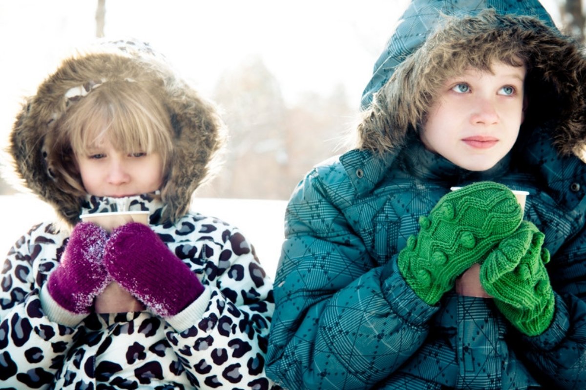 Two kids in warm winter coats and mittens holding warm drinks